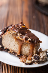 Close up view of a piece of peanut butter chocolate caramel cheesecake pie and cup of coffee on wooden background with a coffee pot and cheesecake in the background. A Sweet Coffee Break concept 