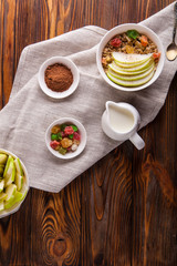 Breakfast bowl of oat granola with apple and dry fruit in a white bowl on brown wooden background  with a yogurt. Copy space
