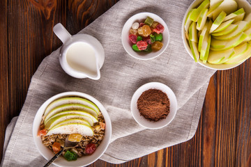 Breakfast bowl of oat granola with apple and dry fruit in a white bowl on brown wooden background  with a yogurt. Copy space