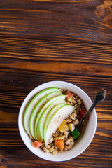 Breakfast bowl of oat granola with apple and dry fruit in a white bowl on brown wooden background  with a yogurt. Copy space