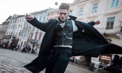 Young man in image of black magician walks on street with magic wand.