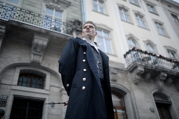 Young man in image of black magician walks on street with magic wand.
