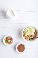 Breakfast bowl of oat granola with apple and dry fruit in a white bowl on white wooden background  with a yogurt. Copy space