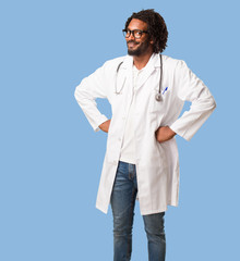 Handsome african american medical doctor with hands on hips, standing, relaxed and smiling, very positive and cheerful