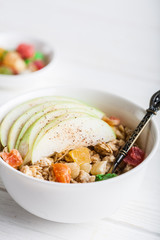 Breakfast bowl of oat granola with apple and dry fruit in a white bowl on white wooden background  with a yogurt. Copy space