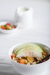 Breakfast bowl of oat granola with apple and dry fruit in a white bowl on white wooden background  with a yogurt. Copy space