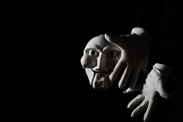 White scary mask on a black background with whites hand.