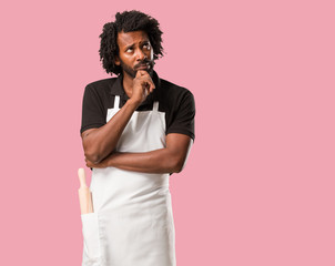 Handsome african american baker doubting and confused, thinking of an idea or worried about something