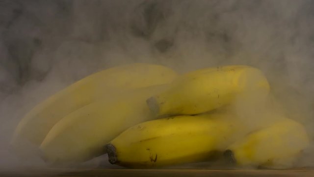 A bunch of fresh bananas on a black background from which comes sweat and cool, smoke, close-up, 4K