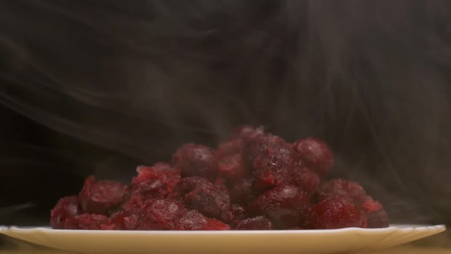 Rotating plate with frozen cherries on a black background, frosty freshness and cold smoke come from the cherry, close-up, 4K