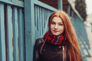 Portrait of young tender redhead young girl with healthy freckled skin wearing knitted scarf looking at camera with serious,pensive expression. Caucasian teen model with ginger hair posing outdoors