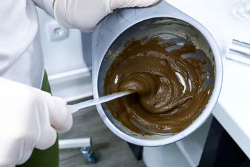 beautician worker in white gloves in beauty salon stirring cosmetic facial mask of sea ​​algae for anti aging and  hydration of skin in plastic bowl with plastic stick, preparation for skin treatment