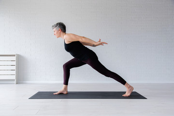 Fototapeta premium Mature Caucasian woman practicing yoga on livingroom floor. Middle aged woman doing yoga indoors.