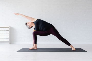 Fototapeta na wymiar Mature Caucasian woman practicing yoga on livingroom floor. Middle aged woman doing yoga indoors.