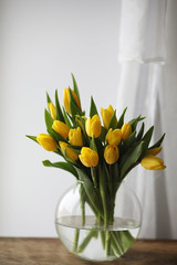 A bouquet of yellow tulips in a vase on the windowsill. A gift to a woman's day from yellow tulip flowers. Beautiful yellow flowers in a vase by window.