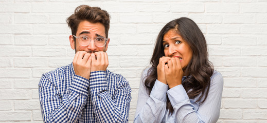 Young indian woman and caucasian man couple biting nails, nervous and very anxious and scared for the future, feels panic and stress