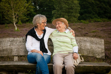 Two senior women sitting on a bench in a park, concept generations, family, care