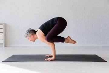Mature Caucasian woman practicing yoga on livingroom floor. Middle aged woman doing yoga indoors.