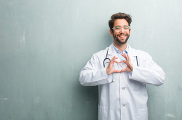 Young friendly doctor man against a grunge wall with a copy space making a heart with hands,...