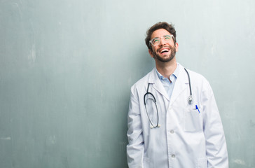Young friendly doctor man against a grunge wall with a copy space laughing and having fun, being relaxed and cheerful, feels confident and successful