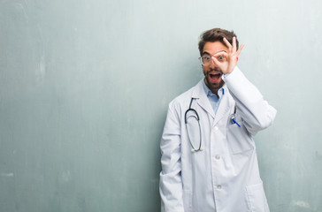 Young friendly doctor man against a grunge wall with a copy space cheerful and confident doing ok gesture, excited and screaming, concept of approval and success