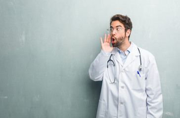 Young friendly doctor man against a grunge wall with a copy space screaming angry, expression of...