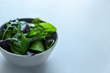 Bowl with mix fresh leaves of arugula, spinach and beet leaves on gray wooden background. Vegetarian food concept. Selective focus.