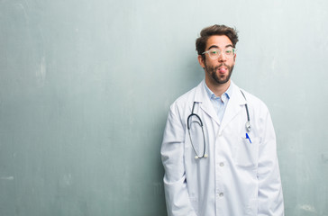 Young friendly doctor man against a grunge wall with a copy space expression of confidence and emotion, fun and friendly, showing tongue as a sign of play or fun