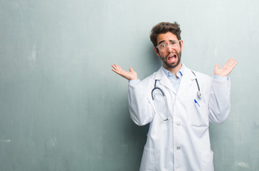 Young friendly doctor man against a grunge wall with a copy space crazy and desperate, screaming...