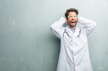 Young friendly doctor man against a grunge wall with a copy space crazy and desperate, screaming out of control, funny lunatic expressing freedom and wild
