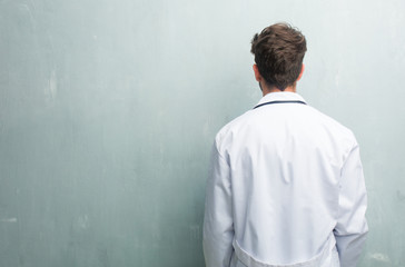 Young friendly doctor man against a grunge wall with a copy space showing back, posing and waiting,...