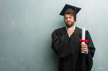 Young graduated man against a grunge wall with a copy space with a sore throat, sick due to a virus, tired and overwhelmed