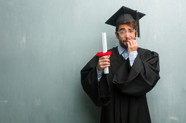 Young graduated man against a grunge wall with a copy space biting nails, nervous and very anxious...