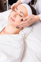 Fototapeta na wymiar beautician giving manual face massage to woman lying on bathrobe and hairband at beauty salon