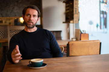 Middle aged caucasian male sitting at the table in coffee shop explaining stuff