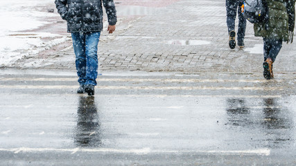 Winter City Slippery Sidewalk. Feet of people walking along the icy snowy pavement in crosswalk in...