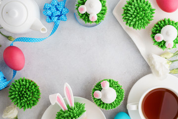 Easter background with bunny cupcakes, tea and painted eggs.