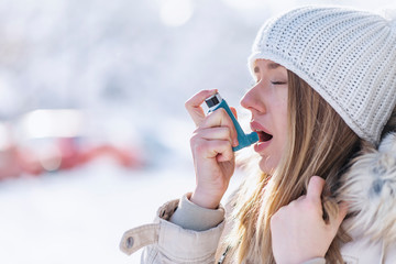 Portrait of a woman using an asthma inhaler in a cold winter with a snowy mountain in the background