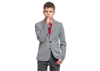 Handsome Teen Boy in suit making Silence gesture - Shh! Portrait of caucasian confident Teenager with finger on his lips  isolated on white background. Serious child looking at camera.