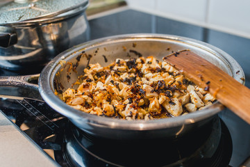 Chicken fillet slices are fried with onions and carrots in a metal frying pan on an induction cooker - close-up - home cooking