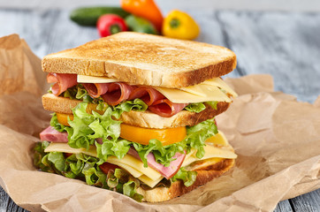 Sandwich with ham cheese on paper, on wooden background