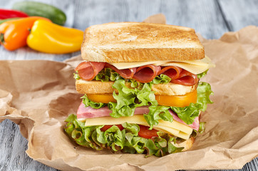 Sandwich with ham cheese on paper, on wooden background