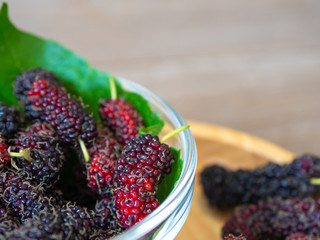 Close up of mulberry with a green leaves in Glass bowl on the wooden plate on wooden table. Mulberry this a fruit and can be eaten in have a red and purple color and delicious and sweet nature.