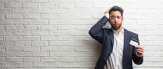 Young business man wearing a suit against a white bricks wall worried and overwhelmed, forgetful,...