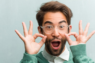 Young handsome entrepreneur man face closeup cheerful and confident doing ok gesture, excited and screaming, concept of approval and success