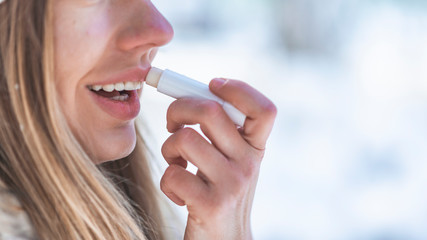 Happy woman applying lip balm in winter holiday in a snowy mountain