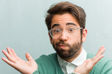 Young handsome entrepreneur man face closeup doubting and shrugging shoulders, concept of...