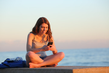 Fototapeta na wymiar Happy student using a smart phone on a bench