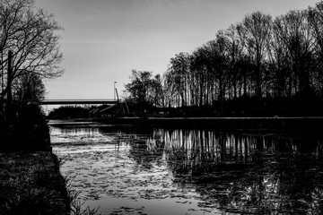 Dramatic and monochrome sunrise over a Beautiful early winter landscape with a frozen river or canal, treelined riverside and grass at sunrise creating a tranquile and quiet scenic nature background