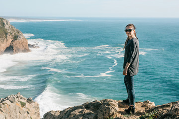 A young beautiful girl on a cliff near the Atlantic Ocean looks and smiles.